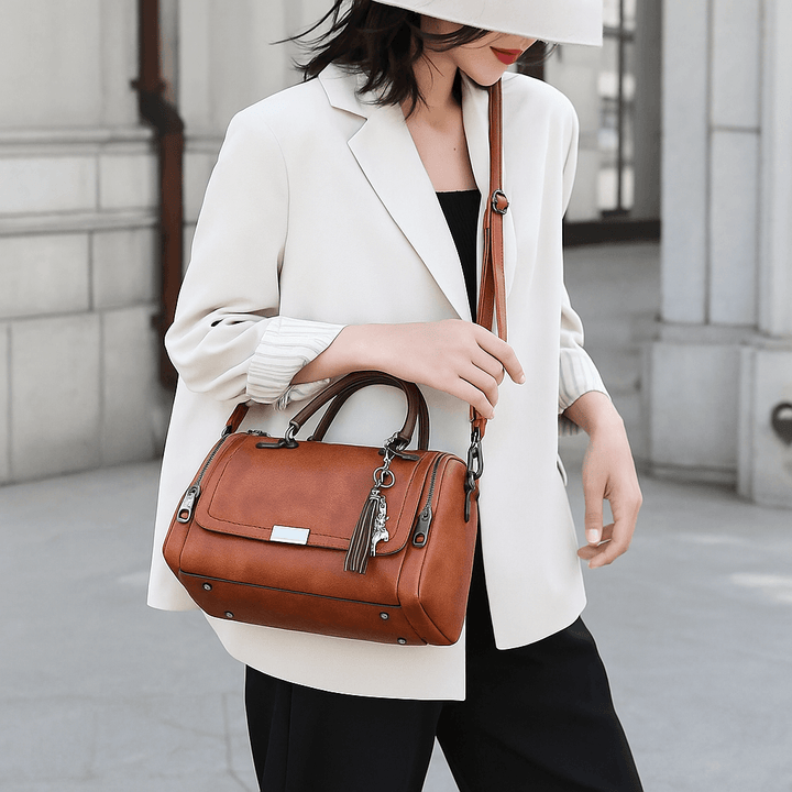 Mulher usando a Bolsa Boston Camel Heritage da RariElla, modelo vintage premium em couro sintético com alça tiracolo, exibida em look elegante ao ar livre.