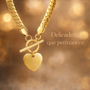 Colar dourado com pingente de coração em cenário sofisticado com luz quente (bokeh), destacando o brilho do aço inoxidável.