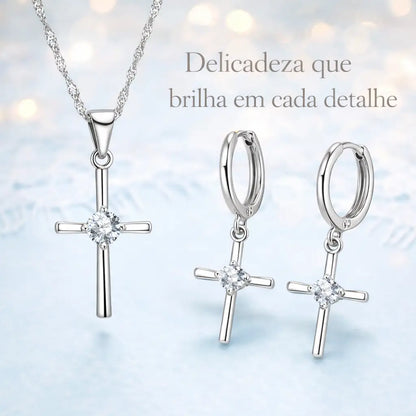 Conjunto Cruz Lumière em Prata 925 com zircônia cristal em cenário suave com texto “Delicadeza que brilha em cada detalhe”