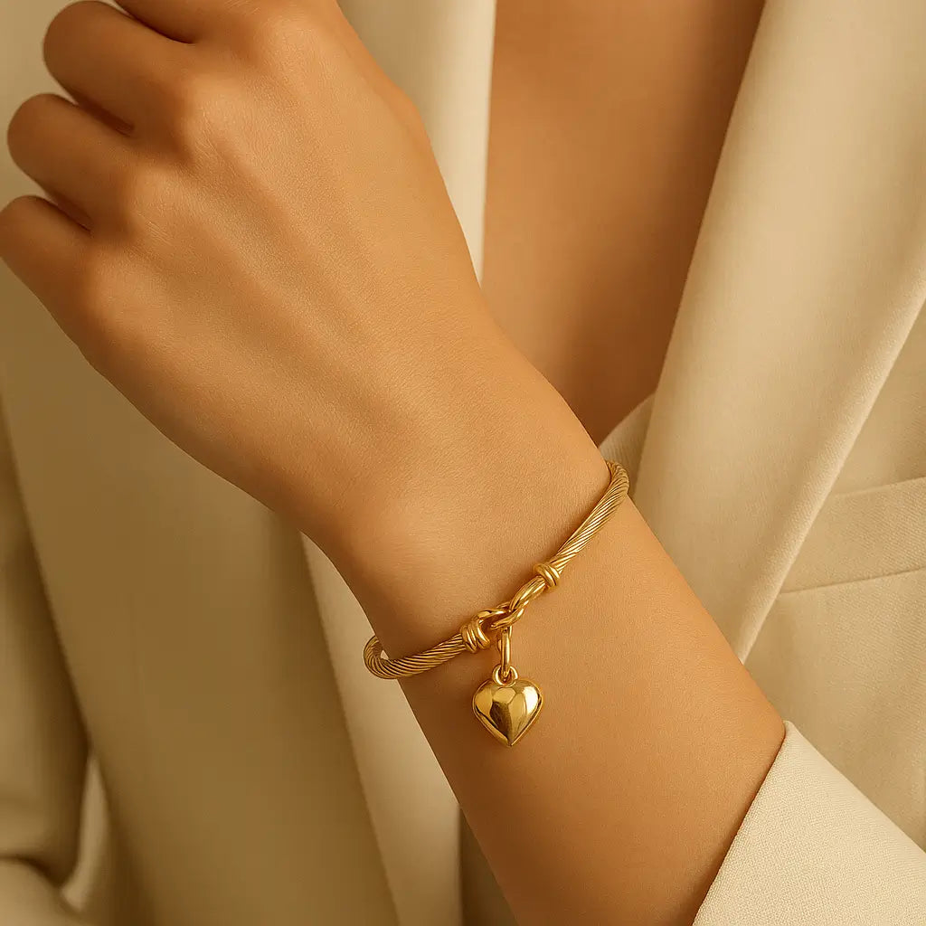 Pulseira feminina dourada com pingente de coração em aço inoxidável, usada no pulso, com design elegante e acabamento premium.